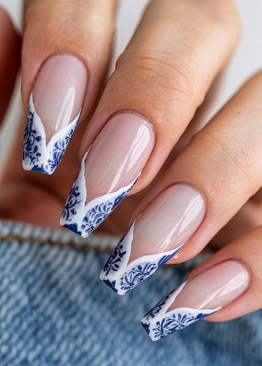 Elegant nail art design featuring intricate blue and white floral patterns on nude nails.