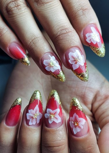 Elegant red stiletto nails with white floral designs and golden accents for a luxurious look.