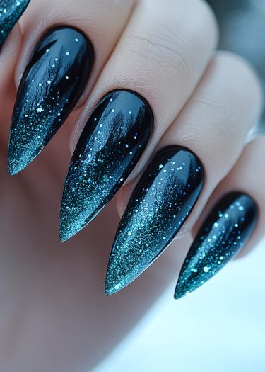 Elegant stiletto nails with black to teal gradient and sparkling glitter for stunning nail art.