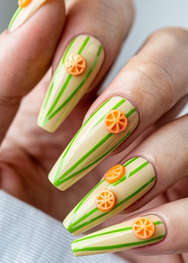 Vibrant stiletto nail art with green stripes and orange slices on pastel yellow base.