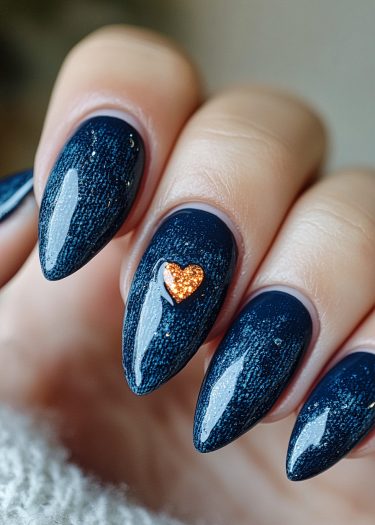 Elegant navy blue almond nails with glittery orange heart embellishment for stylish nail art.