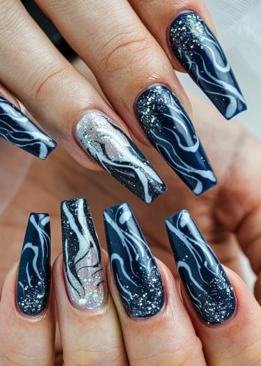 Stylish navy blue coffin nails with white swirls and glitter for a cosmic manicure.