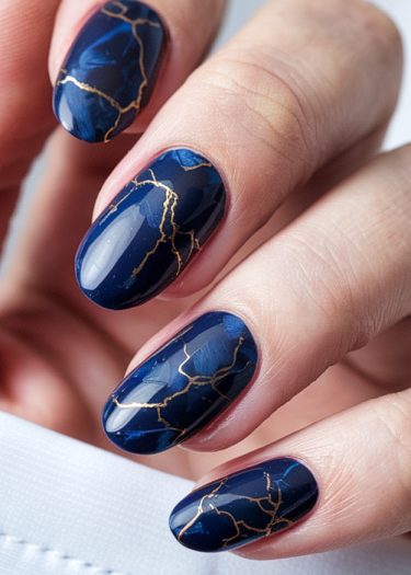 Elegant navy blue nails with gold veining, showcasing exquisite manicure art and sophistication.