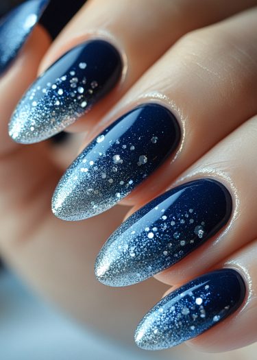 Elegant almond-shaped nails with navy-blue to silver gradient nail art and glitter finish.