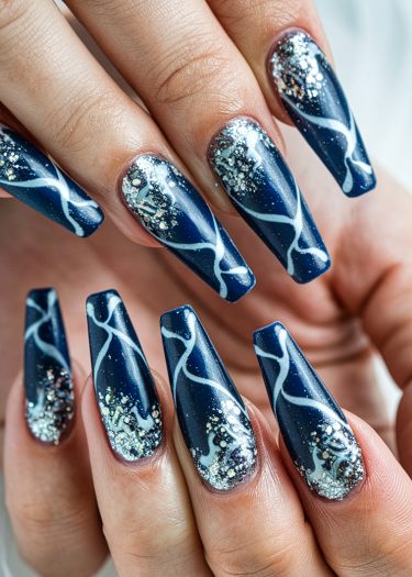 Elegant coffin-shaped navy blue nails with white marbled patterns and sparkling glitter accents.