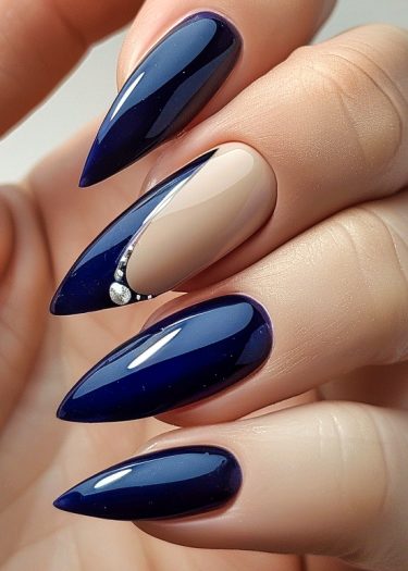 Elegant navy blue stiletto nails with rhinestone accent for a sophisticated manicure design.