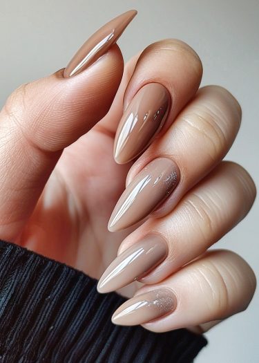 Elegant stiletto nails in glossy taupe with shimmer against a warm-toned hand.