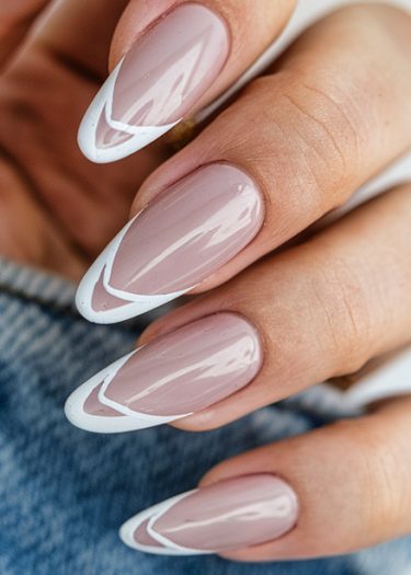 Elegant nude almond nails with artistic French tips on a blurred denim background.