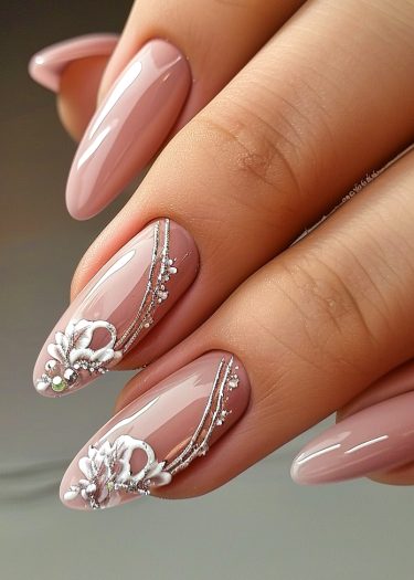 Elegant nude pink almond nails featuring intricate 3D floral art and silver accents.