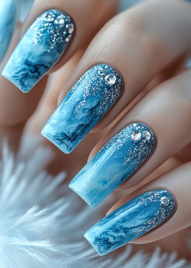 Elegant blue ombre ocean gradient nails with marbling, glitter, and rhinestones for a luxurious manicure.