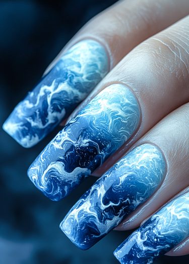 Ocean wave nail art design featuring intricate blue and white patterns on long, manicured nails.