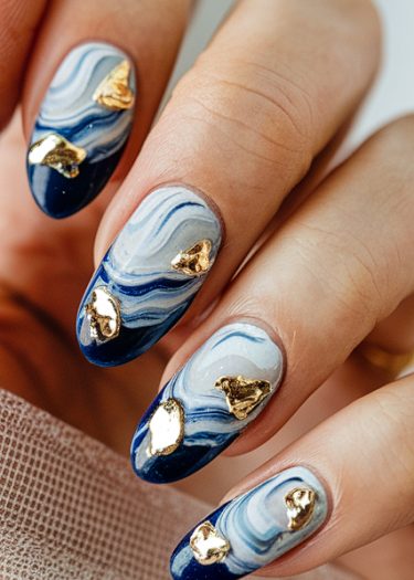 Almond-shaped ocean wave nails with marbled blue and gold foil accents showcase elegant nail art.