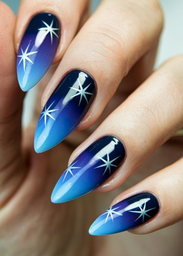 Elegant ombre blue nail art with star design on manicured almond-shaped nails.