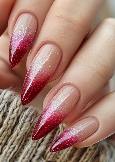 Elegant almond-shaped ombre nails with red to pink gradient and shimmering glitter accents.