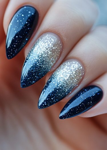 Elegant stiletto nails with navy blue ombre and shimmering silver glitter design.