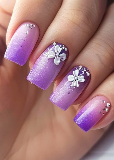 Elegant ombre purple nail art with 3D floral designs and sparkling embellishments for special occasions.