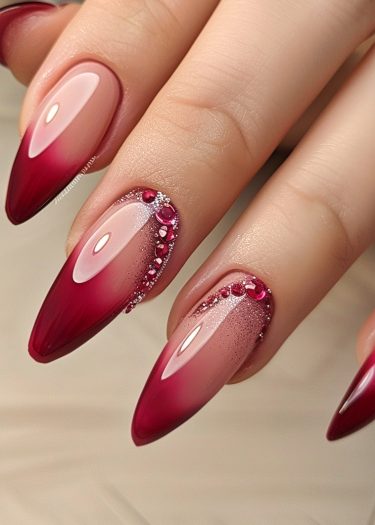 Ombre red almond nails with sparkling rhinestones and glitter for a glamorous, elegant look.