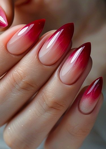 Elegant ombre stiletto nails transitioning from nude pink to rich crimson red.