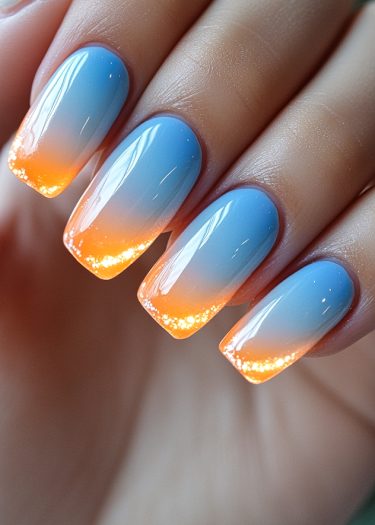 Stunning ombre sunset nails in blue and orange with glossy finish and sparkles.