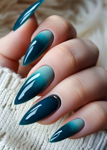 Elegant ombre teal stiletto nails with glitter accent, showcased against a cozy sweater backdrop.