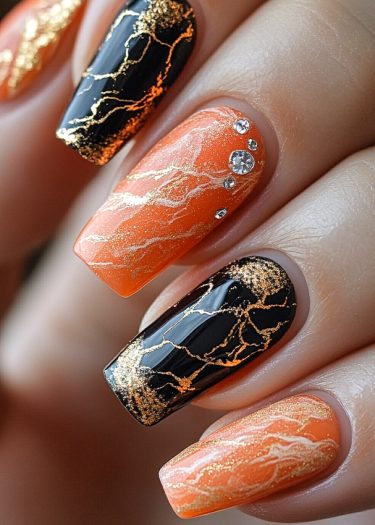 Elegant orange and black nail design with gold marbling and rhinestones for a chic look.