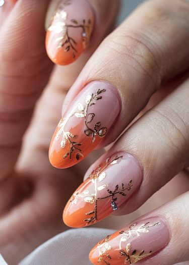 Elegant orange and nude almond nail art with gold botanical designs and a gem accent.