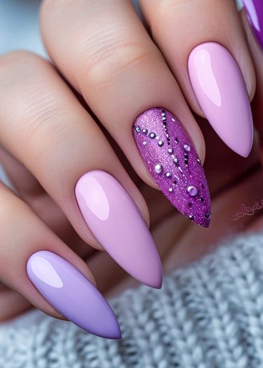 Elegant pink and purple almond-shaped nails with glitter and unique designs on a soft background.