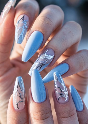 Elegant pastel blue almond nails with creative silver accent designs in a close-up presentation.