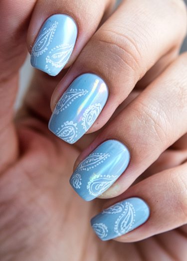 Elegant pastel blue nails with intricate white paisley designs for stylish manicures.