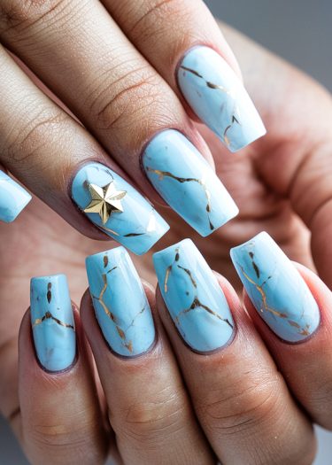 Pastel blue and gold nail art design with elegant marble detailing and a star embellishment.