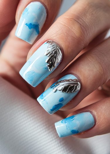 Elegant pastel blue nail art with marbling and metallic feather designs for a sophisticated look.