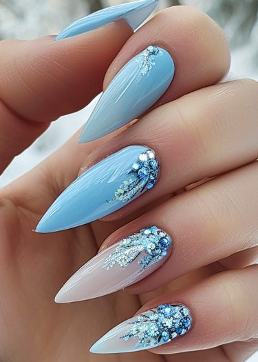 Elegant stiletto nails in pastel blue with intricate ice-inspired designs and sparkling embellishments.