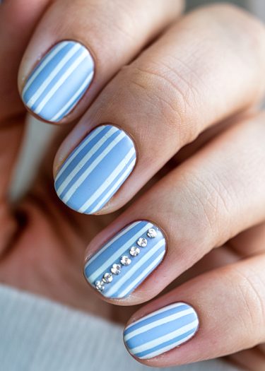 Stylish pastel blue striped nails with rhinestones for a modern manicure look.