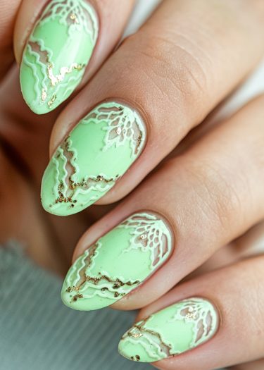 Elegant pastel green almond nails with intricate gold and white marbling designs.