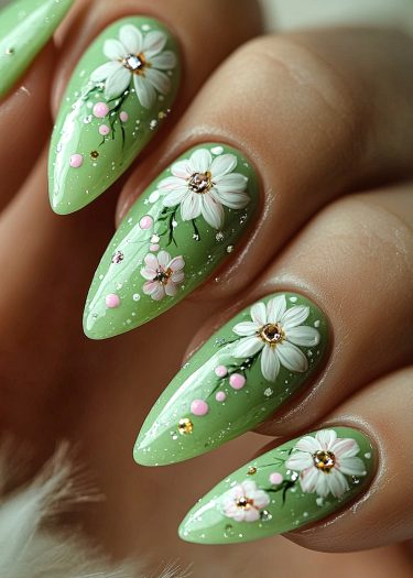 Elegant pastel green stiletto nails adorned with intricate floral designs and sparkling embellishments.