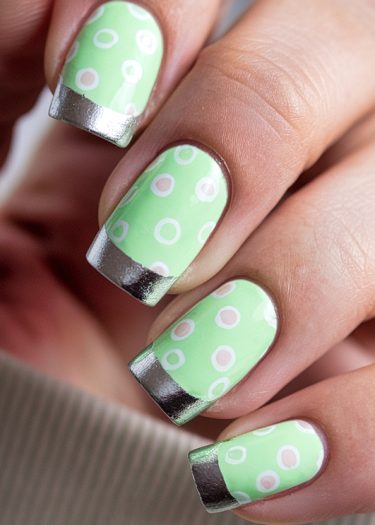 Vibrant pastel green nails with playful polka dots and metallic silver tips, elegantly manicured.