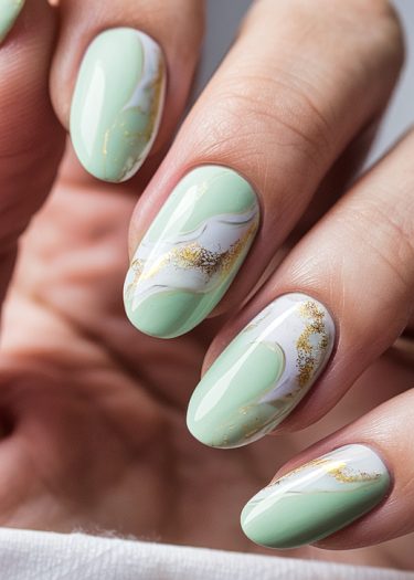 Chic mint green almond-shaped nails with white swirls and gold accents for elegant style.