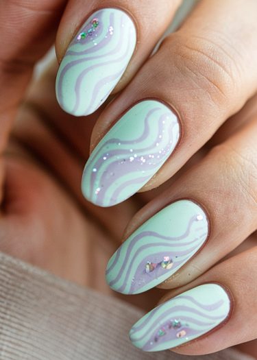 Elegant pastel mint green and lavender nail art with glitter on almond-shaped nails.