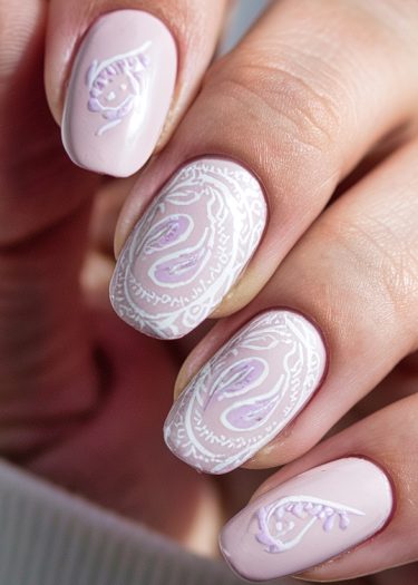 Elegant pastel pink nail art featuring intricate white paisley designs and light purple accents.