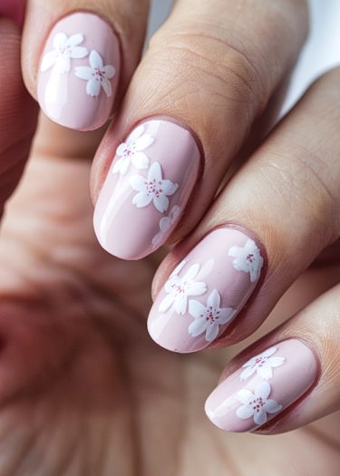 Elegant pastel pink floral nail art with intricate white designs and glossy almond shapes.