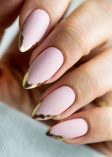 Elegant pastel pink manicure with gold foil accents on almond-shaped nails.