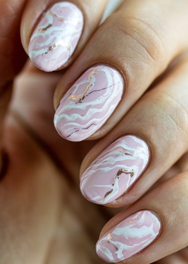 Elegant pastel pink marble nails with gold accents, featuring intricate marble designs and oval shapes.