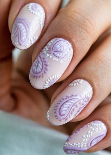 Elegant almond-shaped pastel pink nails with intricate lavender and white paisley nail art.