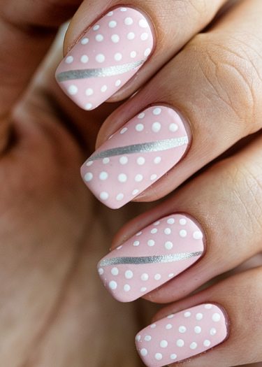 Pastel pink polka dot nails with silver stripes for a chic, elegant manicure.