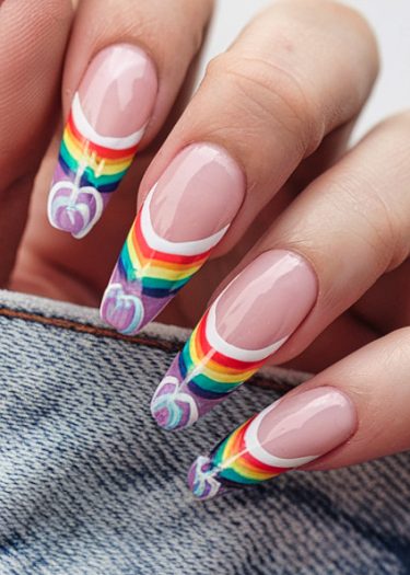 Vibrant rainbow nail art on long almond-shaped nails against denim fabric backdrop.