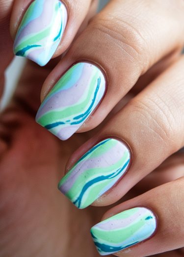 Stylish pastel swirls nail art featuring elegant marbled patterns in blue, green, and lavender.