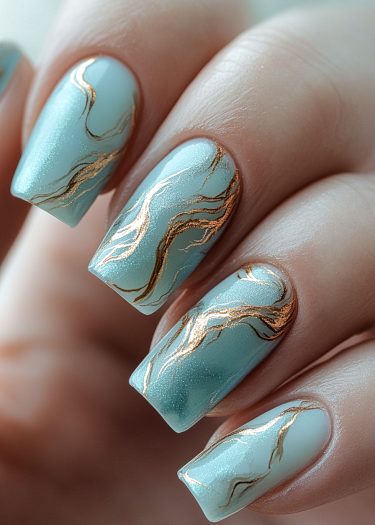 Elegant light blue manicure with gold accents, featuring glossy finish and intricate design.