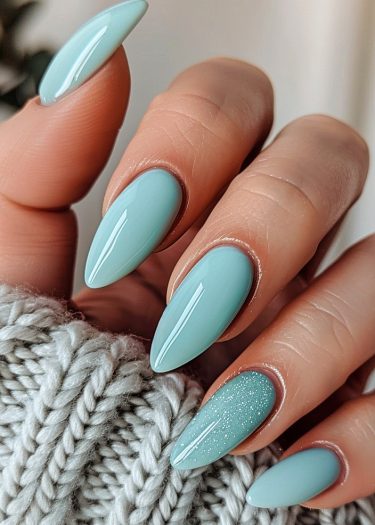 Elegant almond-shaped teal nails with glitter resting on a cozy gray knit sweater.