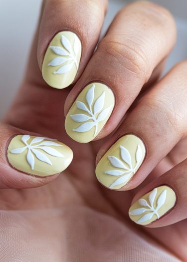 Elegant pastel yellow nail art with intricate white leaf designs for chic style.