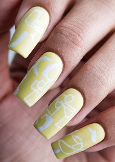 Pastel yellow nail art features unique white abstract designs for a modern, artistic look.